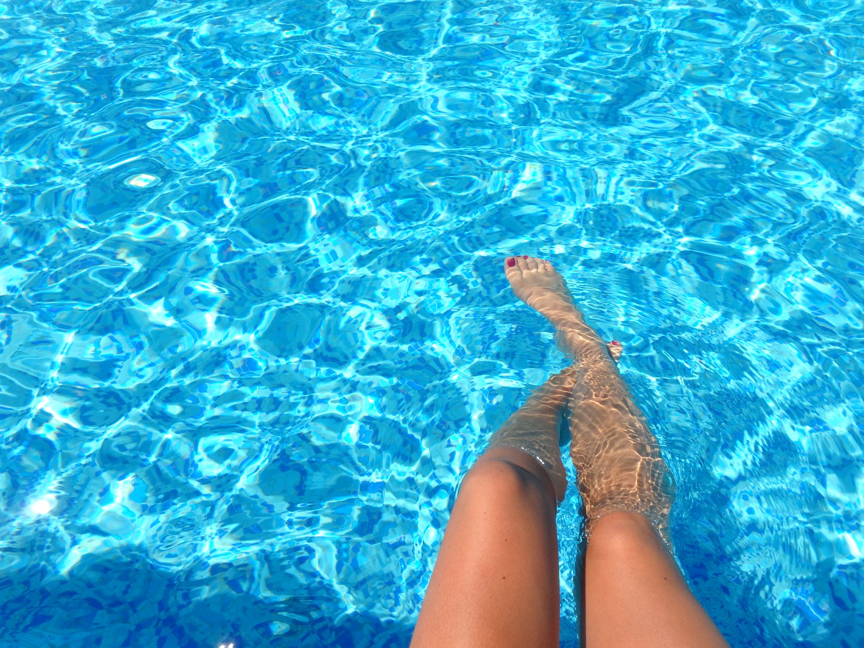 An image of a woman's legs floating in a clear blue swimming pool.